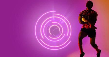 Foto de Jugador de rugby afroamericano sosteniendo pelota por patrón circular iluminado sobre fondo púrpura. Copiar espacio, compuesto, deporte, competición, juego, partido, forma y concepto abstracto. - Imagen libre de derechos