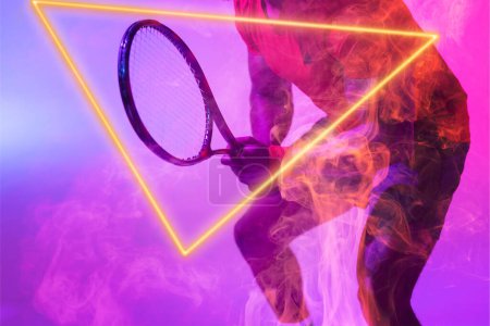 Foto de Sección media del jugador de tenis afroamericano que sostiene la raqueta por triángulo rojo iluminado. Copiar espacio, compuesto, deporte, competencia, forma, juego, partido, mano, humo y concepto abstracto. - Imagen libre de derechos