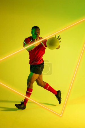 Foto de Jugador masculino afroamericano lanzando pelota de rugby por triángulo iluminado sobre fondo verde. Copiar espacio, compuesto, deporte, competencia, forma, juego, partido y concepto abstracto. - Imagen libre de derechos