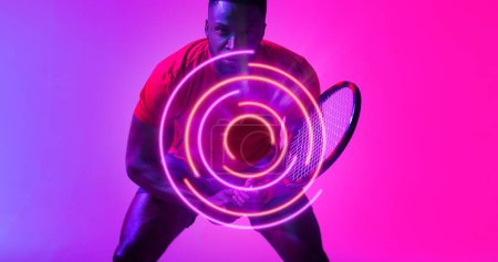 Téléchargez les photos : Modèle circulaire éclairé sur un joueur de tennis afro-américain tenant une raquette sur fond rose. Espace de copie, composite, sport, compétition, jeu, match, forme et concept abstrait. - en image libre de droit