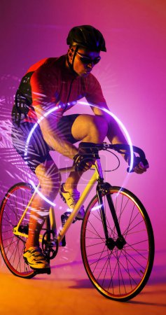 Téléchargez les photos : Cycliste masculin caucasien vélo par cercle éclairé et des plantes sur fond rose. Composite, sport, cyclisme, course, compétition, nature, forme. Casque, lunettes et concept abstrait. - en image libre de droit