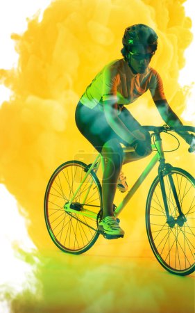 Téléchargez les photos : African american female athlete wearing glasses and helmet riding bike over smoky background. Copy space, yellow, composite, sport, cycling, racing, competition and abstract concept. - en image libre de droit
