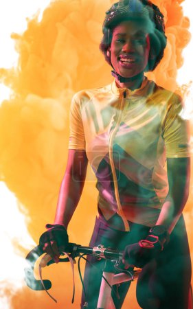 Téléchargez les photos : Portrait d'une athlète afro-américaine portant un casque debout avec un vélo sur fond fumé. Sourire, copier, composite, sport, cyclisme, course, compétition et concept abstrait. - en image libre de droit