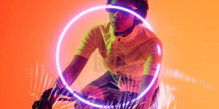 Téléchargez les photos : Midsection of african american female athlete wearing glasses riding bike by circle and plants. Copy space, composite, sport, cycling, racing, competition, nature, shape, illuminated and abstract. - en image libre de droit