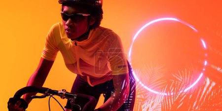 Téléchargez les photos : African american female athlete wearing eyewear riding bike by glowing circle and plants, copy space. Composite, sport, cycling, racing, competition, nature, shape and abstract concept. - en image libre de droit