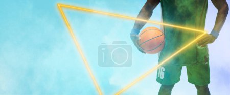 Téléchargez les photos : Midsection of african american player with basketball and hand on hip by triangle on blue background. Copy space, composite, illuminated, sport, competition, illustration, shape and smoke concept. - en image libre de droit