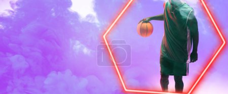 Téléchargez les photos : Midsection of african american basketball player holding ball over hexagon on smoky background. Hand, copy space, composite, illuminated, sport, competition, illustration, shape and abstract concept. - en image libre de droit