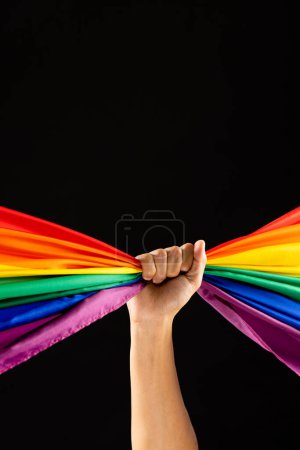 Téléchargez les photos : Main tenant drapeau de couleur arc-en-ciel avec espace de copie sur fond noir. Mois de la fierté, égalité, lgbt et concept des droits de l'homme. - en image libre de droit
