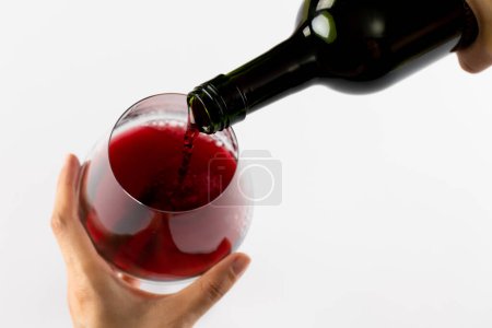 Téléchargez les photos : Mains tenant une bouteille de vin rouge et un verre sur fond blanc, avec espace de copie. Semaine du vin, concept boisson et célébration. - en image libre de droit