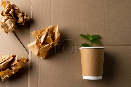 Foto de Close up of pieces of paper and cup with plant on cardboard background with copy space. Global ecology and recycling concept. - Imagen libre de derechos