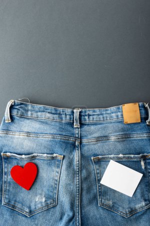 Photo for Vertical jeans with heart and post it lying on grey background. Clothes, fashion, design, fabrics, materials and shopping concept. - Royalty Free Image