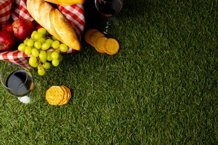 Foto de Picnic basket with food and vichy cloth lying on green grass. Picnic, food, eating outside, relaxing in nature concept. - Imagen libre de derechos