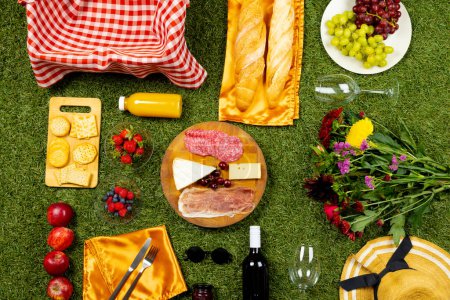 Foto de Cesta de picnic con tela vichy y diversos alimentos que se encuentran en la hierba verde. Picnic, comida, comer fuera, relajarse en el concepto de la naturaleza. - Imagen libre de derechos