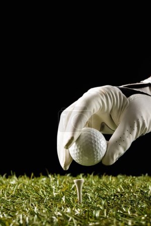 Téléchargez les photos : Close up of hand in white glove putting golf ball on tee on grass with copy space. Golf, sports and competition concept. - en image libre de droit