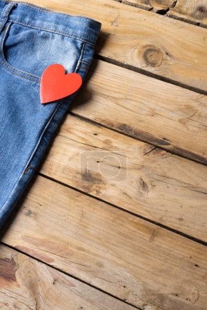 Photo for Vertical image of jeans with heart lying on wooden surface. Clothes, fashion, design, fabrics, materials and shopping concept. - Royalty Free Image