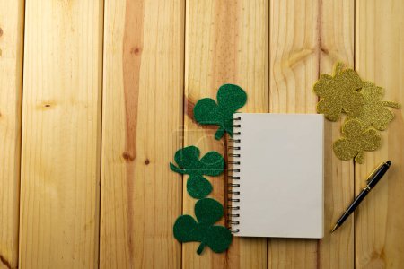 Foto de Imagen de trébol verde y cuaderno blanco con espacio para copiar sobre fondo de madera. Día de San Patricio, tradición irlandesa y concepto de celebración. - Imagen libre de derechos
