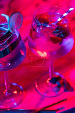 Photo pour Gros plan des verres avec de l'eau et des fruits sur une planche de bois au-dessus des néons. Cocktail et concept de célébration. - image libre de droit