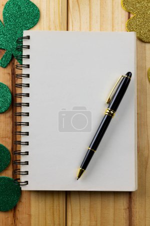 Téléchargez les photos : Image of green clover and white notebook with copy space on wooden background. St patrick's day, irish tradition and celebration concept. - en image libre de droit