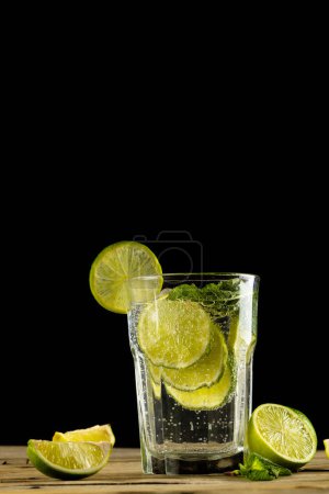 Téléchargez les photos : Glass with water and limes on wooden background with copy space over black background. Cocktail day and celebration concept. - en image libre de droit
