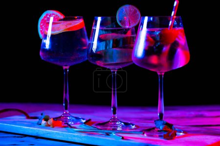 Téléchargez les photos : Three glasses with water and fruit on wooden board over black background. Cocktail day and celebration concept. - en image libre de droit