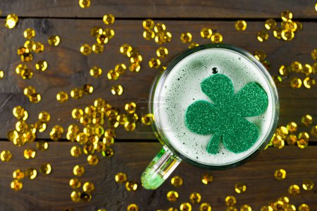 Téléchargez les photos : Image de verre à bière, trèfle et confettis d'or sur fond en bois. Saint-Patrick, tradition irlandaise et concept de célébration. - en image libre de droit