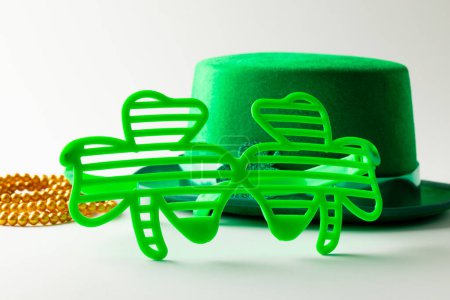 Foto de Image of green hat, green clover glasses, gold necklace and copy space on white background. St patrick's day, irish tradition and celebration concept. - Imagen libre de derechos