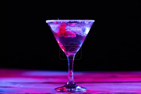 Photo for Glass with water and diverse fruits in neon light with copy space over black background. Cocktail day and celebration concept. - Royalty Free Image