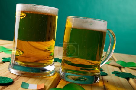 Foto de Imagen de vasos de cerveza, trébol y bandera de Irlanda sobre fondo de madera. Día de San Patricio, tradición irlandesa y concepto de celebración. - Imagen libre de derechos