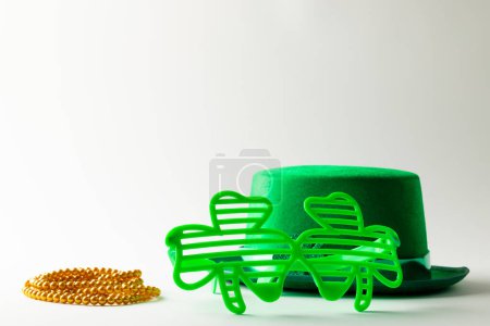 Foto de Image of green hat, green clover glasses, gold necklace and copy space on white background. St patrick's day, irish tradition and celebration concept. - Imagen libre de derechos