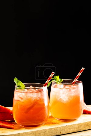 Foto de Glasses with cocktail and straws on wooden board with copy space over black background. Cocktail day and celebration concept. - Imagen libre de derechos