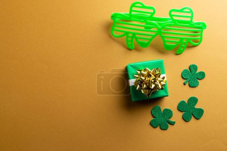 Photo for Image of green glasses, green clover, green present and copy space on orange background. St patrick's day, irish tradition and celebration concept. - Royalty Free Image