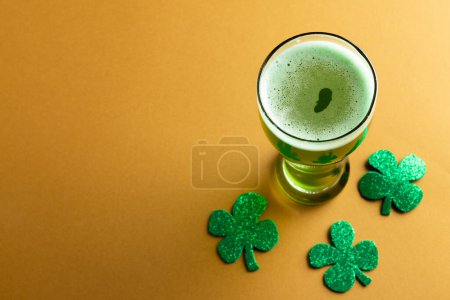 Foto de Image of glass with green beer, clover and copy space on orange background. St patrick's day, irish tradition and celebration concept. - Imagen libre de derechos