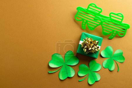 Photo for Image of green clover glasses, green clover, green present and copy space on orange background. St patrick's day, irish tradition and celebration concept. - Royalty Free Image