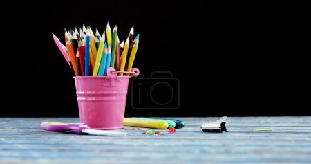 Foto de Close up of colourful pencils in bucket on wooden table on black background. Education and school items concept. - Imagen libre de derechos