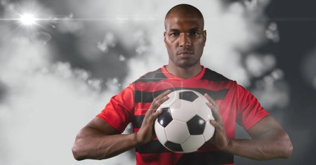 Photo for African american male soccer player holding football against light spot on grey background. sports tournament and competition concept - Royalty Free Image