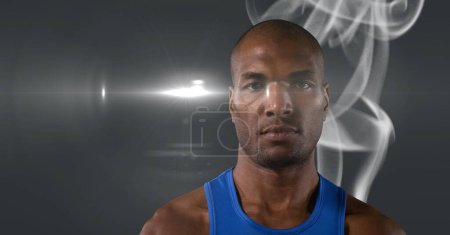Téléchargez les photos : Portrait de l'athlète afro-américain masculin contre l'effet de fumée et la tache lumineuse sur fond gris. tournoi sportif et concept de compétition - en image libre de droit