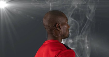 Téléchargez les photos : Rear view of african american male athlete against smoke effect and light spot on grey background. sports tournament and competition concept - en image libre de droit