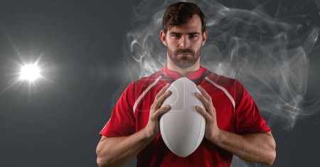 Photo for Portrait of caucasian male rugby player holding ball against smoke and light spot on grey background. sports tournament and competition concept - Royalty Free Image
