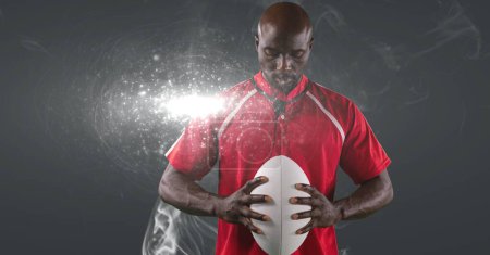 Photo for African american male rugby player holding ball against smoke and light spot on grey background. sports tournament and competition concept - Royalty Free Image