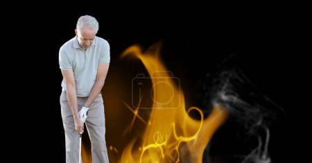 Téléchargez les photos : Blanc senior joueur de golf masculin tenant club contre l'effet de flamme de feu sur fond noir. sport à la retraite et mode de vie actif senior concept - en image libre de droit