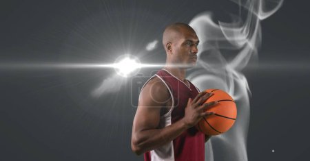 Foto de Jugador de baloncesto afroamericano que sostiene la pelota contra el humo y la mancha de luz sobre fondo gris. torneo deportivo y concepto de competición - Imagen libre de derechos