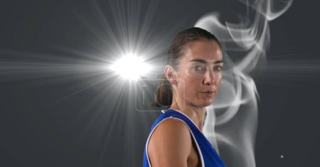 Foto de Portrait of caucasian female athlete against smoke effect and light spot on grey background. sports tournament and competition concept - Imagen libre de derechos
