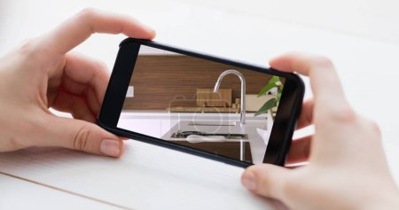 Photo pour Image de la personne utilisant un smartphone avec des intérieurs de cuisine de la maison affichée à l'écran. Achats en ligne maison décoration concept composite numérique. - image libre de droit