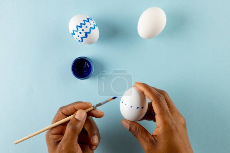 Foto de Imagen de manos de mujer afroamericana pintando huevos de Pascua con espacio para copiar sobre fondo azul. Pascua, religión, tradición y concepto de celebración. - Imagen libre de derechos
