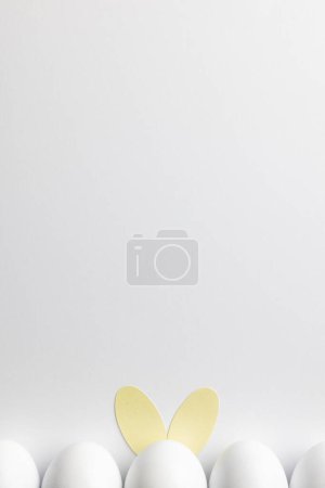 Téléchargez les photos : Image d'une rangée d'œufs de Pâques blancs avec des oreilles de lapin et un espace de copie sur fond blanc. Pâques, religion, tradition et concept de célébration. - en image libre de droit