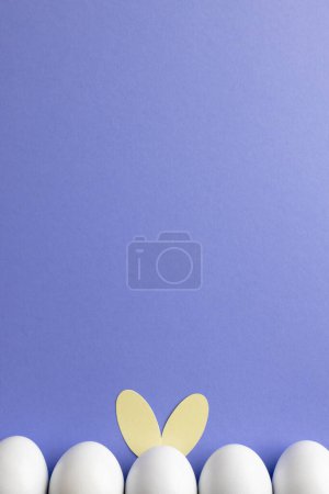 Téléchargez les photos : Image d'une rangée d'œufs de Pâques blancs avec des oreilles de lapin et un espace de copie sur fond violet. Pâques, religion, tradition et concept de célébration. - en image libre de droit