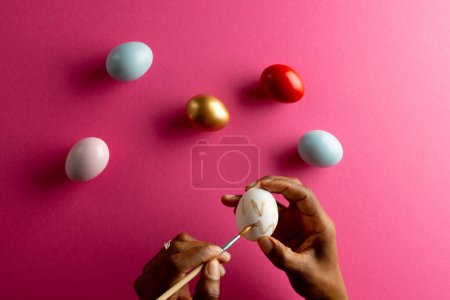 Photo for Image of hands of african american woman painting easter eggs with copy space on pink background. Easter, religion, tradition and celebration concept. - Royalty Free Image