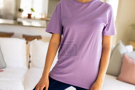 Téléchargez les photos : Intersection de la femme biraciale portant un t-shirt violet avec espace de copie dans le salon. Mode, design, couleur et concept de vêtements. - en image libre de droit