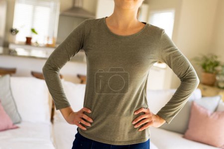 Téléchargez les photos : Milieu de la femme biraciale portant chemise à manches longues grise avec espace de copie dans le salon. Mode, design, couleur et concept de vêtements. - en image libre de droit