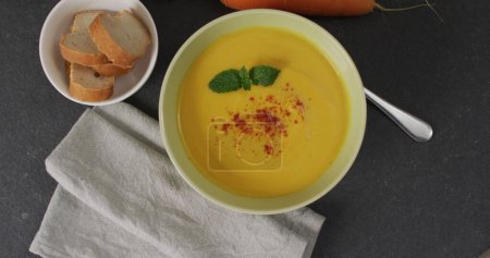 Foto de Cierre de tazón blanco de sopa de zanahoria con pan, servilleta y zanahorias sobre fondo oscuro. Comida y sopa casera. - Imagen libre de derechos